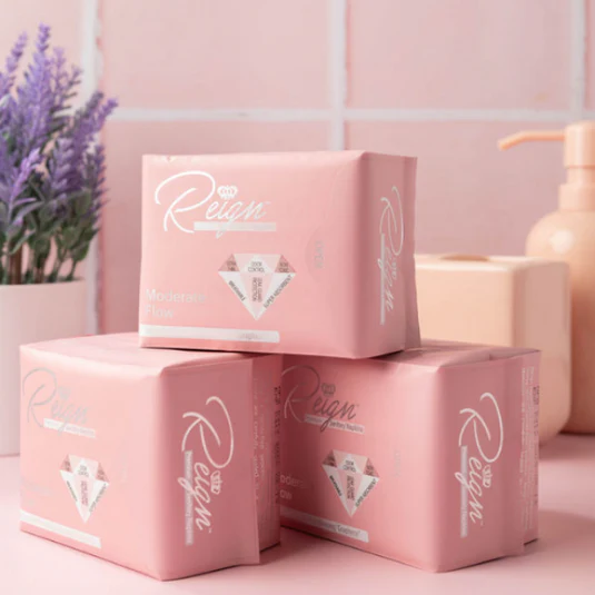 A detailed, photorealistic image showcasing a woman relaxing at home, using vegan sanitary pads. The setting should be warm and inviting, with elements like a cozy blanket and herbal tea, symbolizing comfort. The pads should be subtly visible, highlighting their natural qualities.